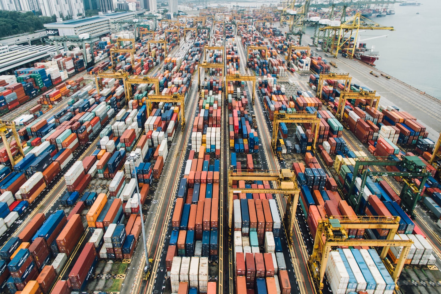 Widok z lotu ptaka na ruchliwy port kontenerowy z dźwigami bramowymi i statkami.