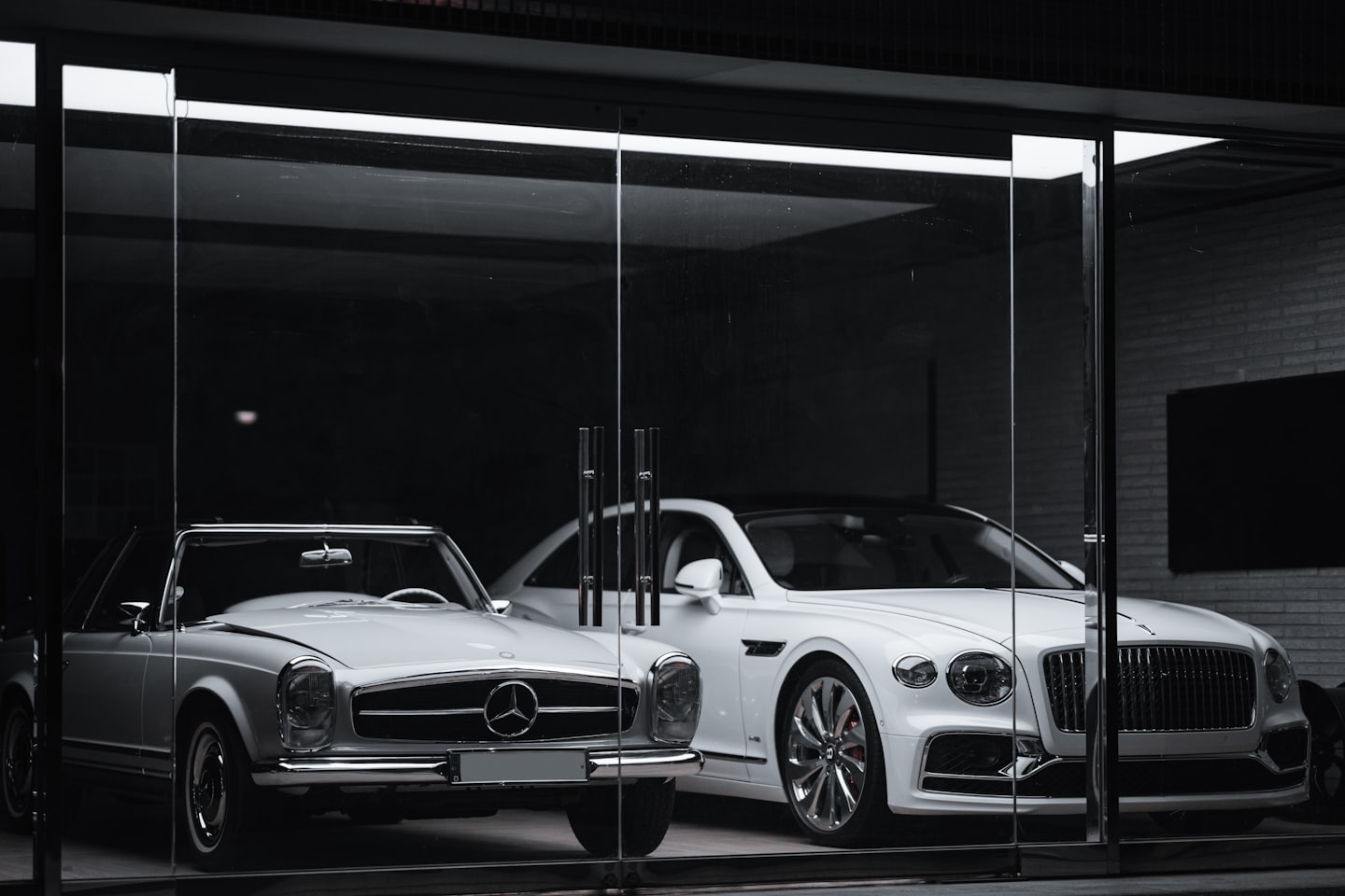 Biały, zabytkowy Mercedes i nowoczesny Bentley zaparkowane w salonie samochodowym.